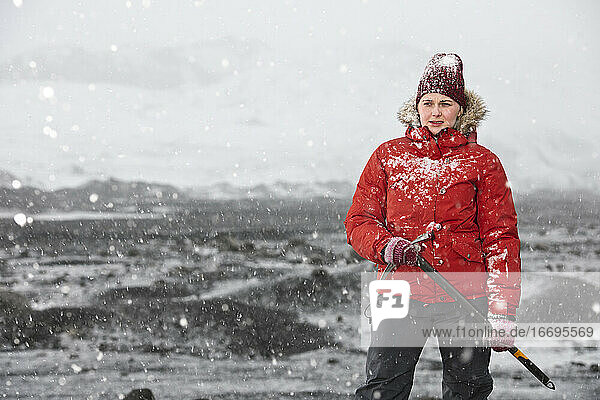 Frau steht und hält Eispickel in der Nähe eines Gletschers in Island