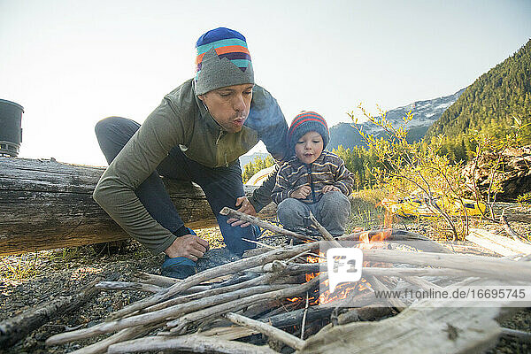 Vater und Sohn arbeiten zusammen  um auf einem Campingplatz in der Wildnis ein Feuer zu machen.