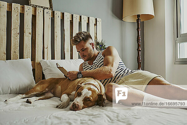 Ein junger blonder Junge liest im Bett mit seinem Hund