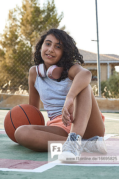 Nahaufnahme eines sitzenden Mädchens mit lockigem Haar mit einem Basketball und Kopfhörern