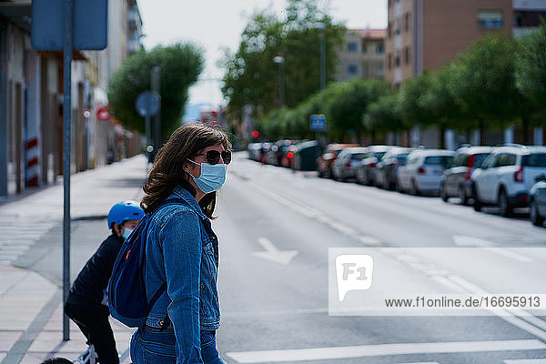 Frau auf der anderen Straßenseite mit einer Maske und Sonnenbrille