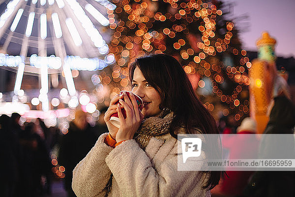 Fröhliches Teenager-Mädchen trinkt Glühwein auf dem Weihnachtsmarkt