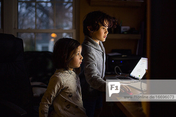 Zwei Kinder stehen in einem dunklen Raum  dessen Gesichter von einem Computerbildschirm beleuchtet werden.