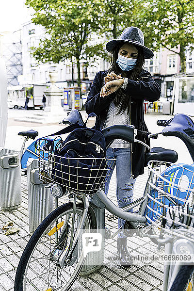 Young woman with mask chooses bicycle at a public rental point