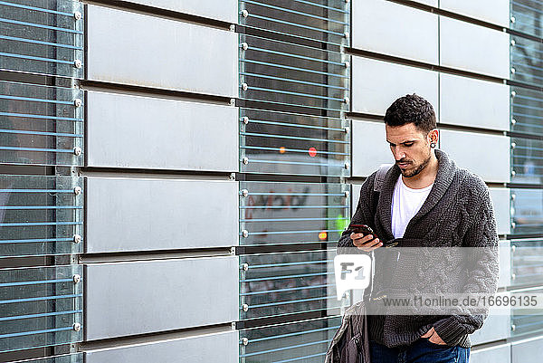 Junger bärtiger Mann  der auf der Straße geht und dabei ein Smartphone benutzt