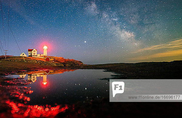 Lighthouse reflecting in water under the Milkyway night sky.