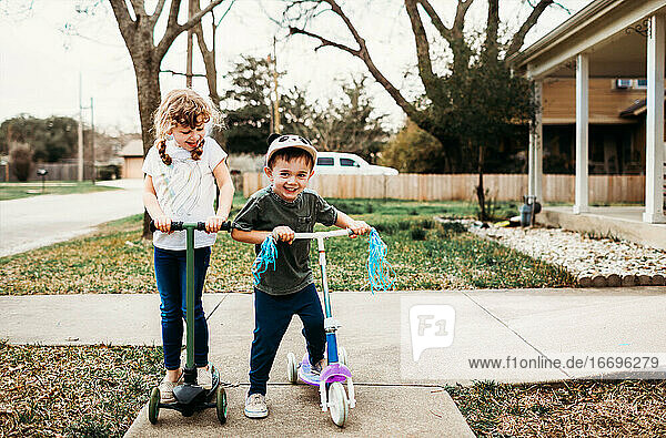 Junge Brüder und Schwestern fahren Roller im Vorgarten