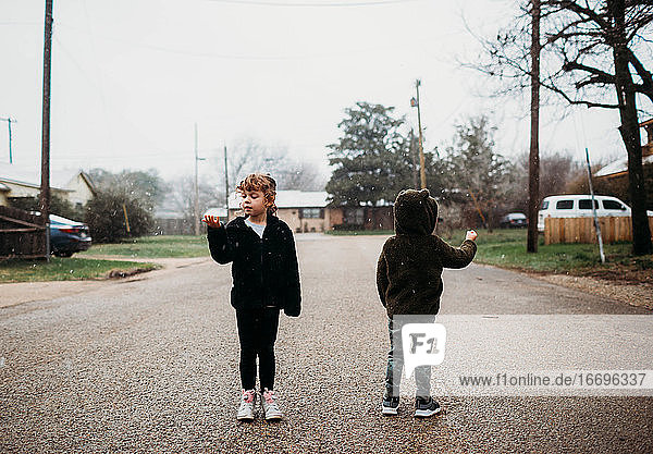 Junger Bruder und Schwester stehen auf der Straße und fangen Schneeflocken
