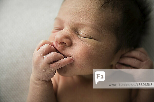 Nahaufnahme eines Details  neugeborenes Baby mit vielen Haaren  das an seinen Fingern saugt