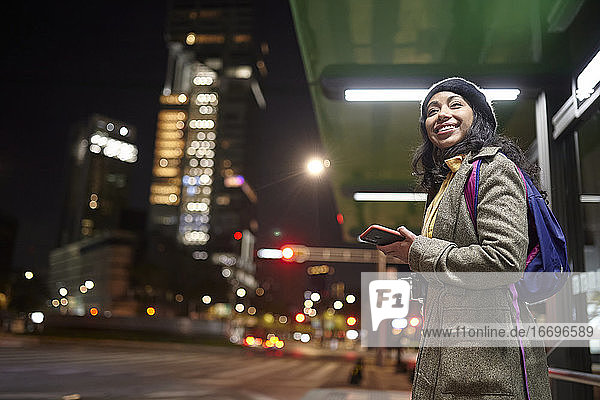 lächelnde Frau  die nachts auf der Straße steht und sein Handy benutzt