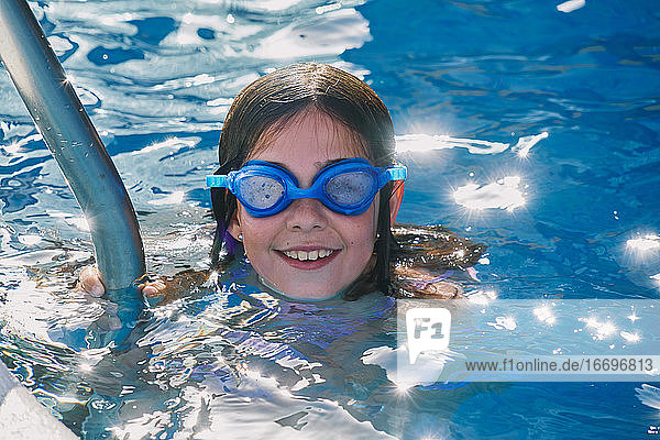 Happy smiling girl swimming and having fun in the pool with blue water