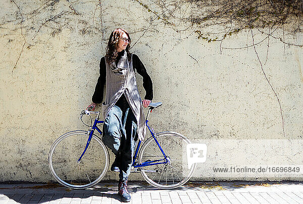 Young woman leaning on a city wall with vintage bike in sunny day