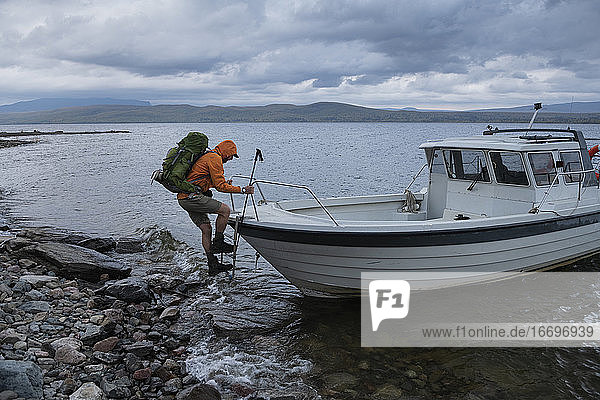 Hiker climbs about small boat ferry across lake Riebnes on Kungsleden Trail  Lapland  Sweden