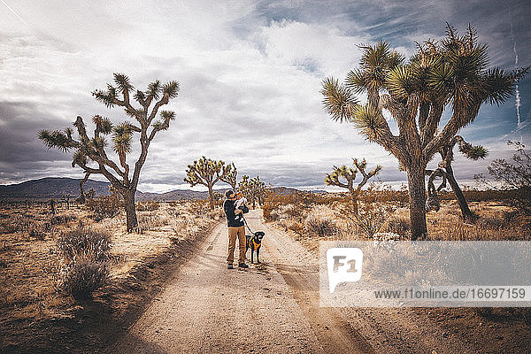 Ein Mann mit einem Baby und einem Hund steht in der Wüste von Kalifornien