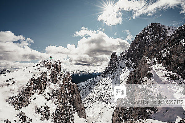 Landschaftsaufnahme einer Bergsteigerin auf einem Gipfel vor blauem Himmel