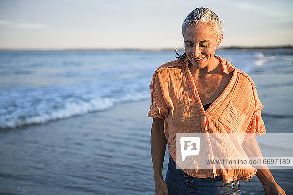 Grauhaarige Frau genießt den Strand bei Sonnenuntergang
