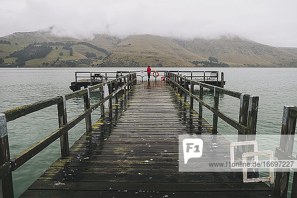 Woman on a red jacket standing at Port Levy Jetty  Banks Peninsula  NZ