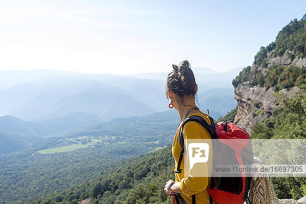 Rückansicht einer jungen Frau  die auf einem hohen Berg steht und die Aussicht betrachtet