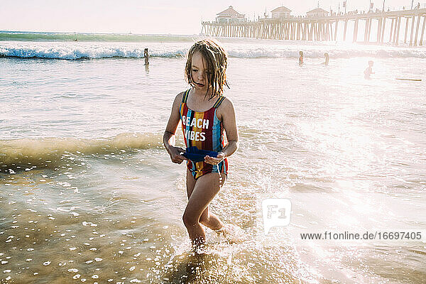 young girl running through water at the beach with pier in background