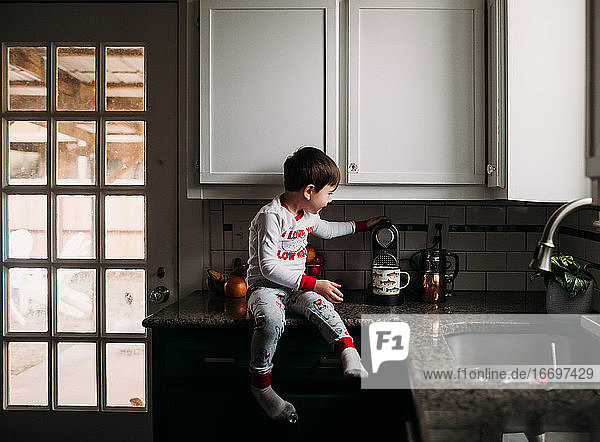 Young boy sitting on kitchen counter learning to use coffee maker