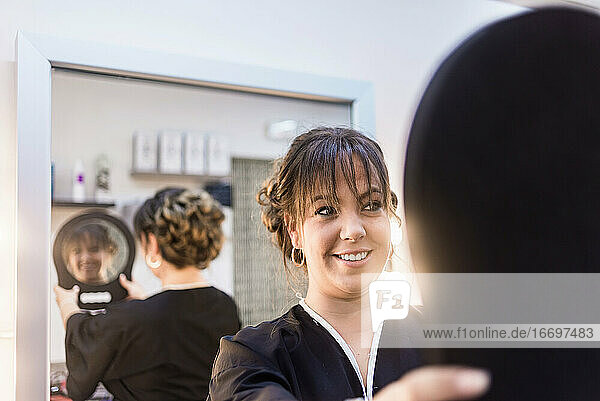 Lächelnde Frau  die sich im Friseursalon im Spiegel betrachtet