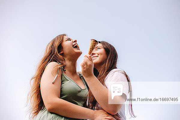 Junge Frau lacht  während sie ihre Freundin gegen den Himmel umarmt