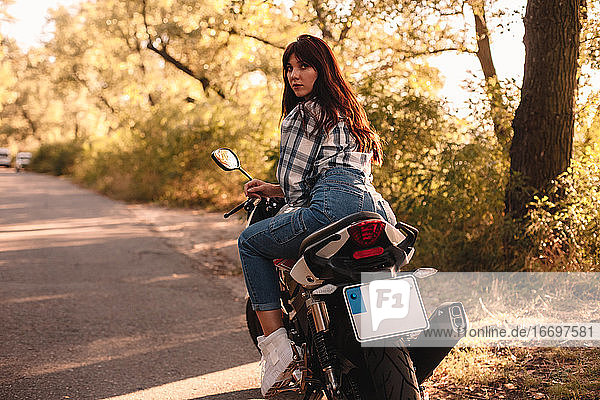 Junge Frau schaut über die Schulter  während sie auf einem Motorrad sitzt