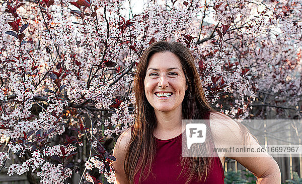 Porträt einer glücklichen Frau vor blühenden Bäumen in einem Garten.