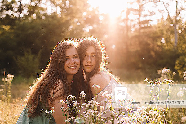 Porträt eines glücklichen lesbischen Paares  das im Sommer inmitten von Blumen sitzt