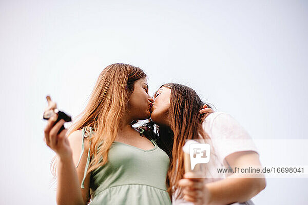 Happy lesbian couple kissing standing against sky in summer