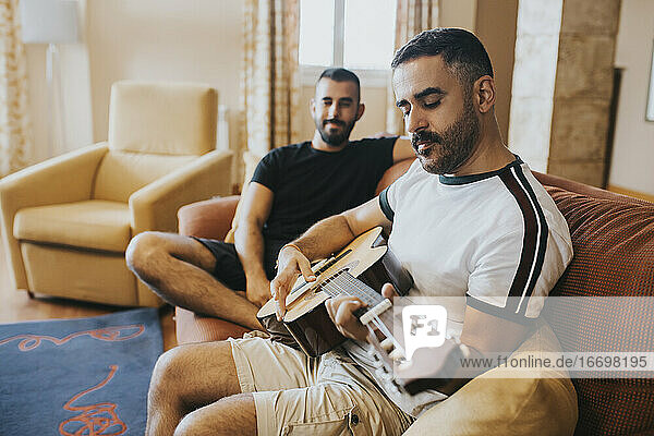 Schwuler Junge beobachtet seinen Freund beim Gitarrenspiel auf dem Sofa