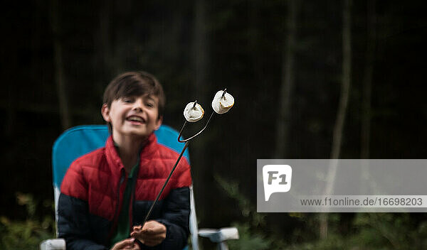 Fröhlicher Junge  der geröstete Marshmallows an einem Metallstab betrachtet.