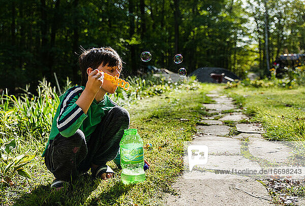 Young boy blowing soap bubbles with a large wand outdoors.