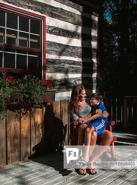 Mother and son sitting in rocking chair on deck of a rustic log cabin.