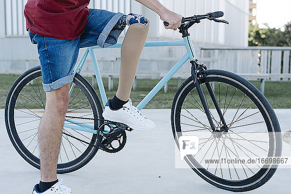 Junger Mann mit Behinderung und Beinprothese fährt Fahrrad auf der Straße
