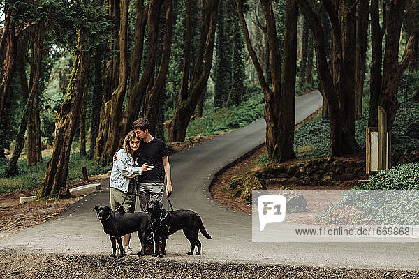 Paar  das sich umarmt  während es mit Hunden auf dem Waldweg steht