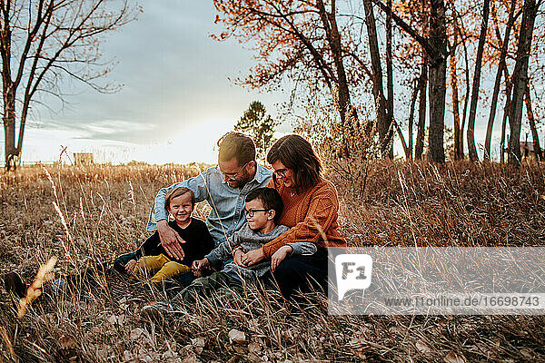 smiling young family snuggling in a field on a fall evening
