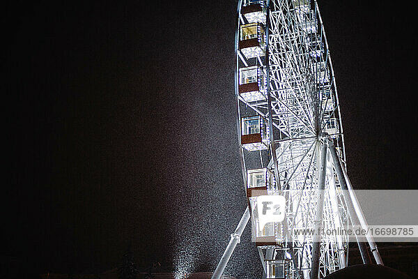 Beleuchtetes Riesenrad in der nächtlichen Winterstadt bei Schneefall