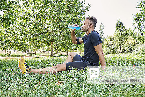 Man drinking sports drink after training. He is in an outdoor park.