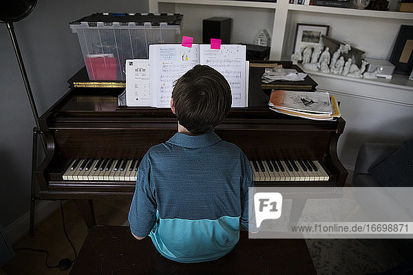 Rückansicht eines Tween Boy  der zu Hause Klavier spielt  von markierten Seiten im Buch