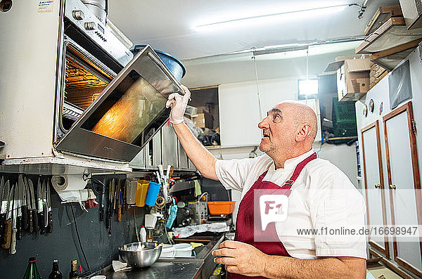Ältere Erwachsene beim Öffnen eines Ofens in der Küche einer Bäckerei in Serbien