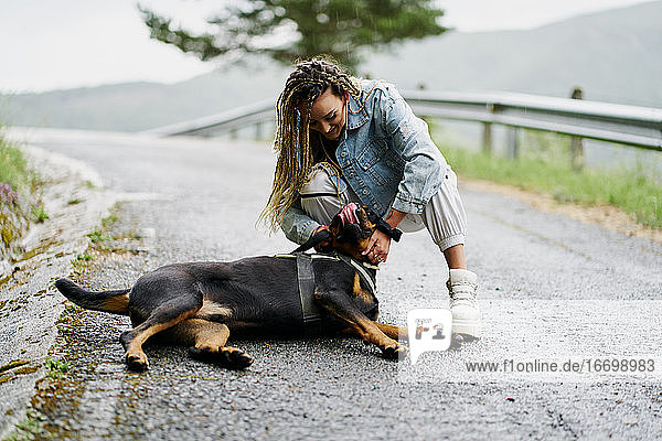 Junge Frau mit blondem geflochtenem Haar  Jeansjacke und weißer Jeans  die an einem regnerischen Tag neben ihrem Hund posiert