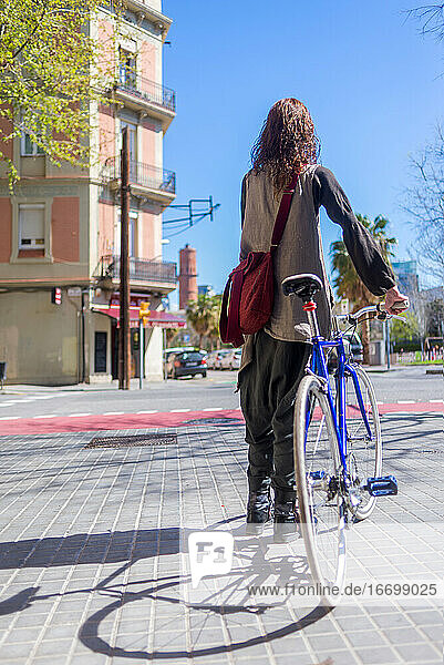 Rückenansicht einer lächelnden Frau  die mit ihrem Fahrrad auf einer Straße in der Stadt spazieren geht