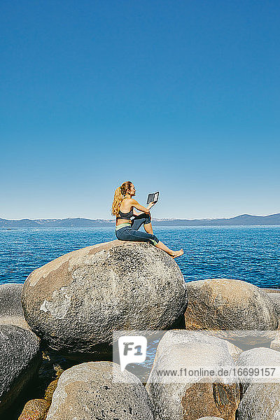 Junge Frau sitzt am Lake Tahoe und liest tagsüber ein Kindle-Buch