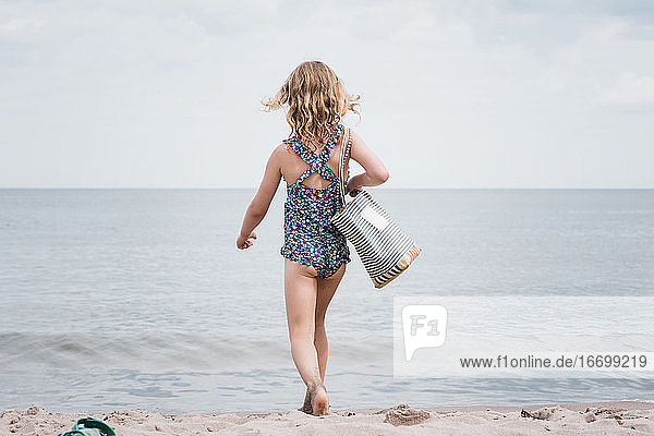 junges Mädchen mit einer Strandtasche in der Hand stolziert zum Meer