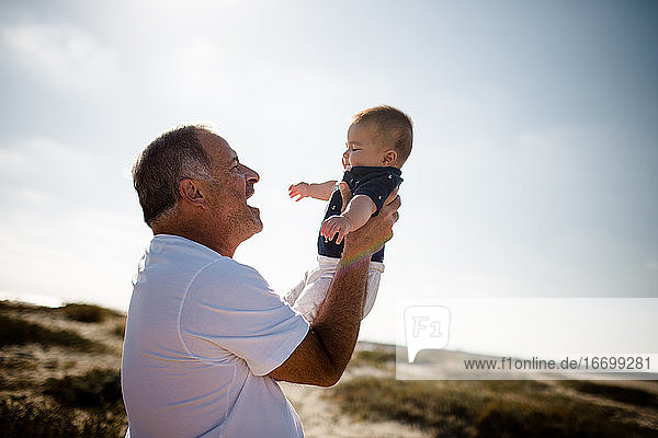 Großvater hält Enkel am Strand stehend