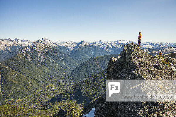 Mann auf einem Berggipfel mit Blick auf den Wald und die Gipfel.