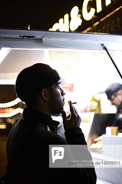 Dunkle Silhouette eines rauchenden Mannes im Licht eines Ladens