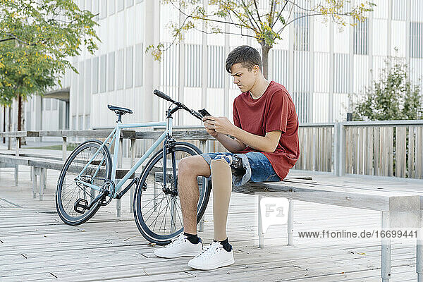 Mann mit Behinderung benutzt Smartphone in der Nähe des Fahrrads