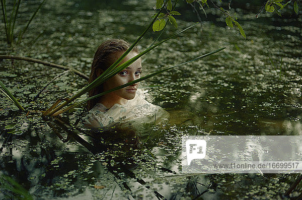 Eine Frau in einem weißen Kleid auf der Oberfläche eines Sumpfwassers im Wald